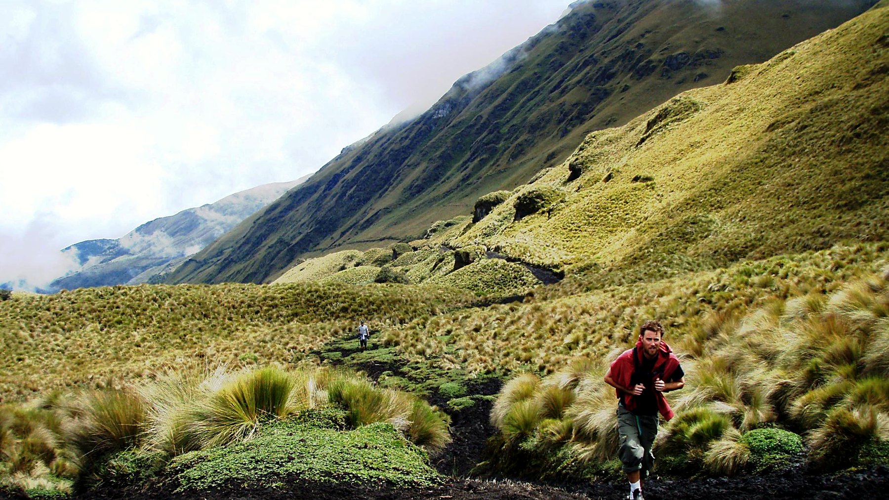 Walking a trail through high-altitude tussock grassland below a cloud-covered ridge